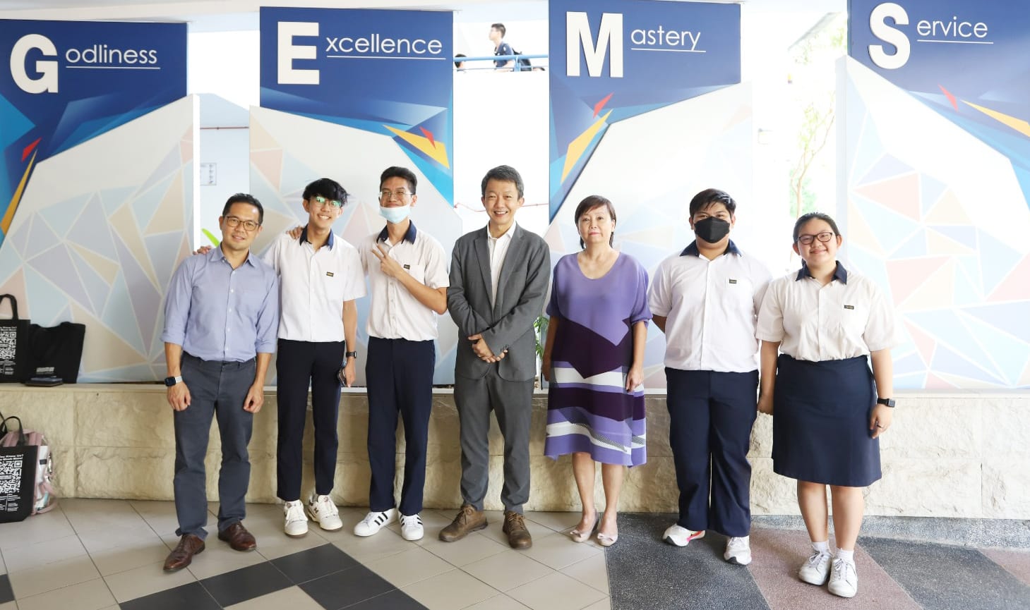 Seven people pose in front of a wall displaying the words Godliness, Excellence, Mastery, and Service.